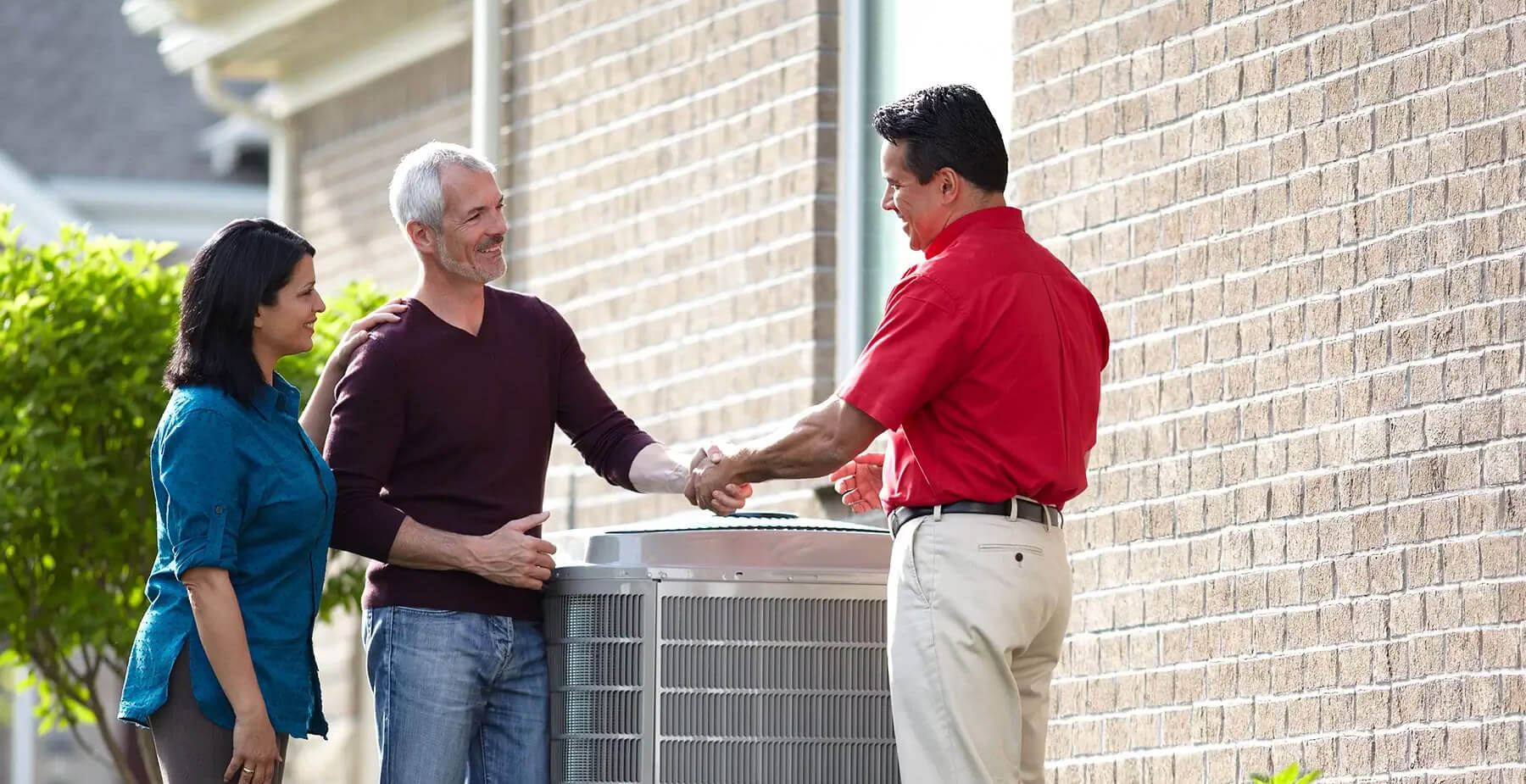 HVAC tech shaking hands with two homeowners standing over a new heat pump.