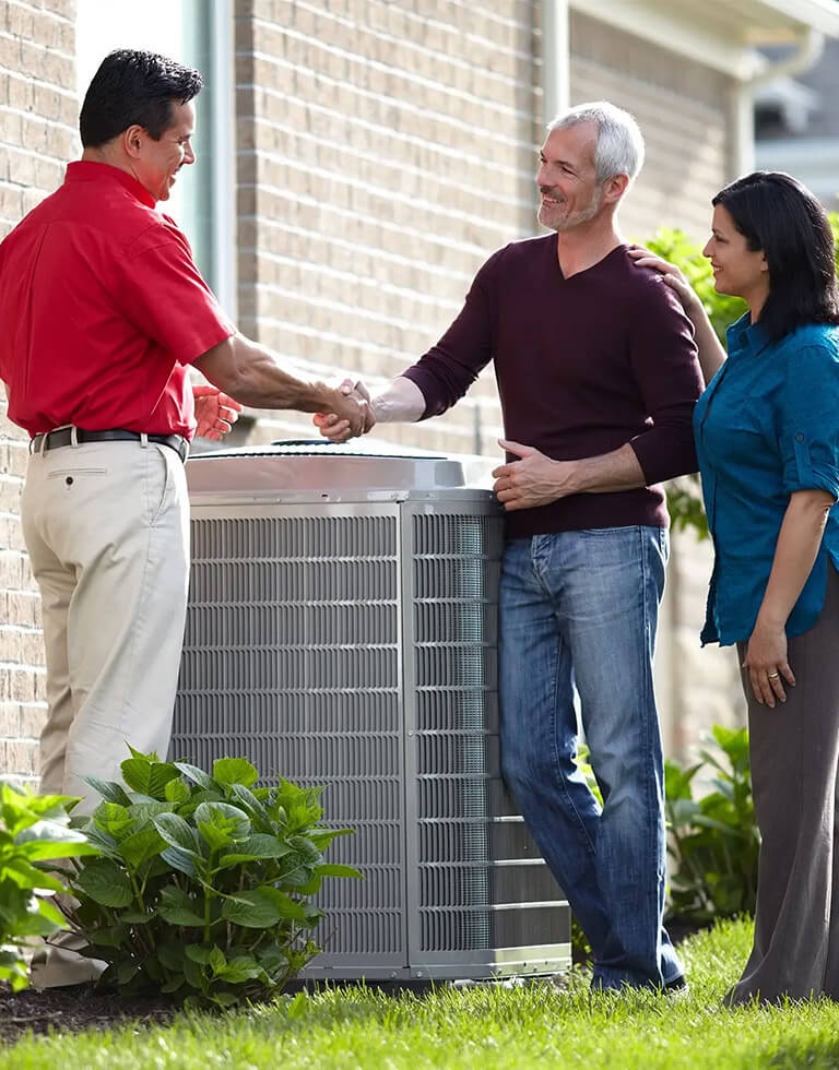 HVAC tech shaking hands with two homeowners standing over a new heat pump.