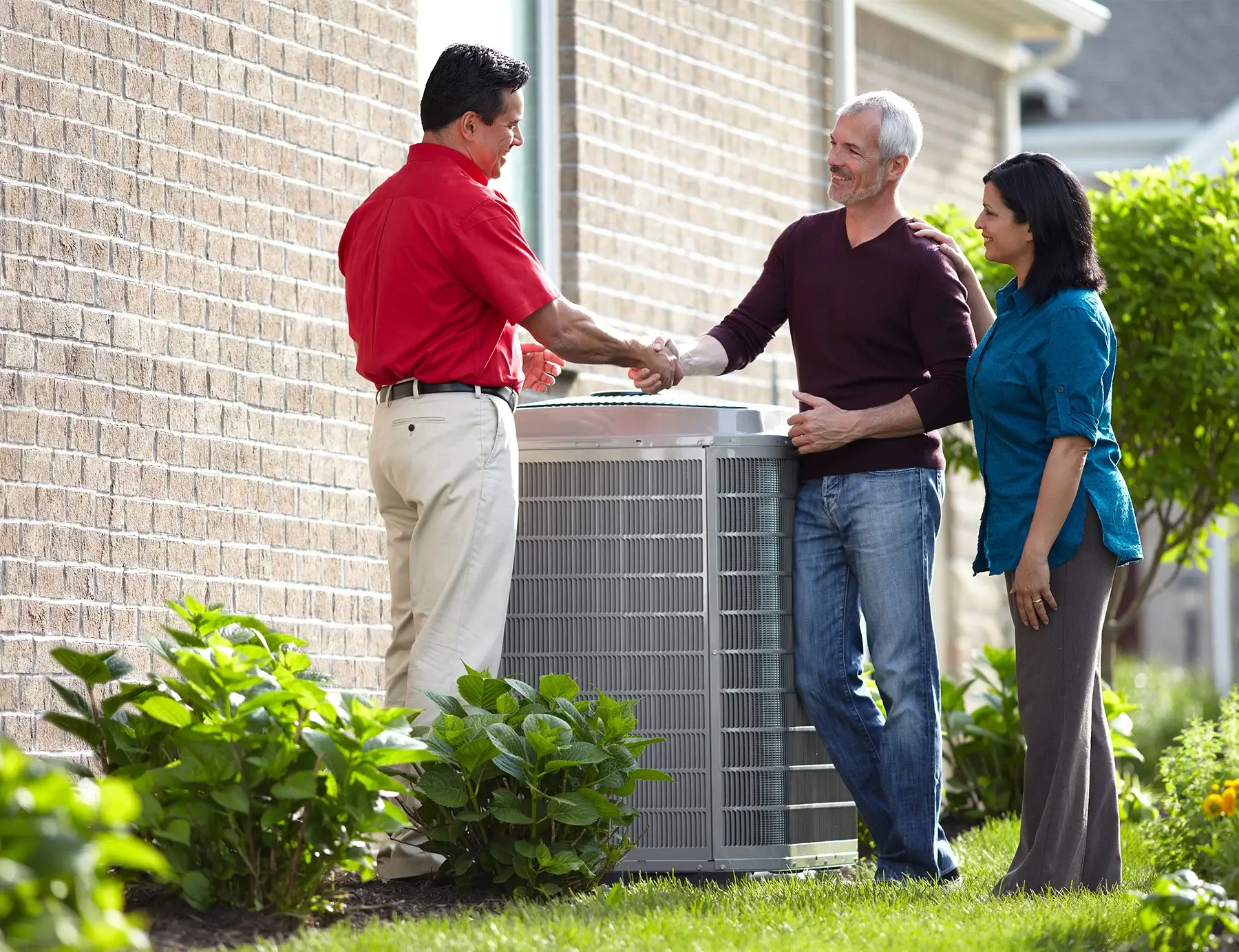 HVAC tech shaking hands with two homeowners standing over a new heat pump.